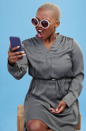 Téléchargez les photos : Téléphone, nouvelles et femme noire en colère choqué en studio frustré par glitch, 404 ou arnaque sur fond bleu. Smartphone, échouer et modèle féminin africain ennuyé par notification, phishing ou spam e-mail. - en image libre de droit