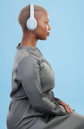 Téléchargez les photos : Écouteurs, musique et profil de la femme noire sur fond bleu pour le podcast de bien-être, se détendre et se détendre. Profil, technologie et personne africaine en streaming audio, écouter la radio et la chanson en studio. - en image libre de droit