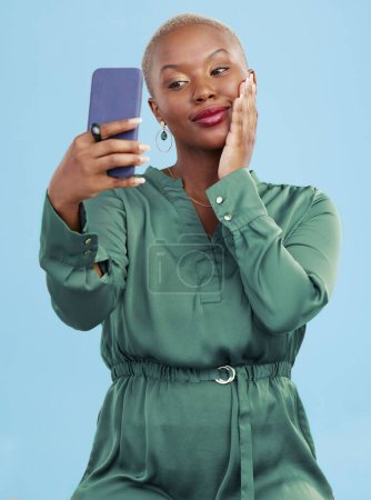 Téléchargez les photos : Sourire, selfie et heureuse femme noire pour mobile app appel vidéo isolé en fond bleu studio avec prix. Connexion, calme et personne, créateur de contenu ou influenceur diffusion en direct sur les médias sociaux. - en image libre de droit