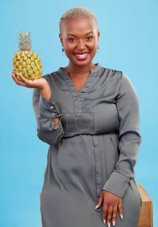 Téléchargez les photos : Femme africaine, ananas et portrait studio pour le choix, la santé et la nutrition par fond bleu. Fille, fruits et heureux avec la décision pour l'alimentation, manger et les aliments végétaliens pour la digestion, vitamines ou fibres. - en image libre de droit