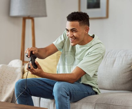 Foto de Hombre feliz, videojuegos y jugar en el sofá con controlador en la sala de estar para un divertido partido en línea en casa. Joven hombre disfrutando de tiempo de juego en la consola para la competencia amistosa o esports en casa. - Imagen libre de derechos