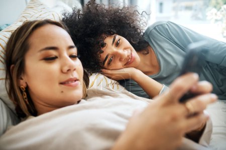 Photo for Phone, social media and an lgbt couple in bed together in the morning for communication or to relax. Love, lesbian and a woman watching a movie or video with her girlfriend in the home bedroom. - Royalty Free Image