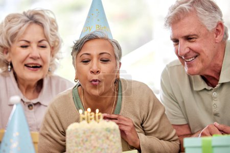 Téléchargez les photos : Femme âgée, amis et gâteau d'anniversaire pour bougies, souhait et excité par la célébration dans la maison de soins infirmiers. Groupe de personnes âgées, personnes et ensemble pour la fête, l'événement et le souffle de la flamme avec la retraite. - en image libre de droit