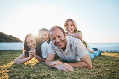 Photo for Family, parents and portrait of children on grass by ocean for bonding, relationship and relax together. Nature, sunlight and happy mother, father and kids on holiday, vacation and travel by sea. - Royalty Free Image