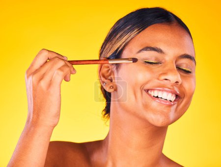 Photo for Woman, eye makeup and beauty with face, brush for cosmetology and cosmetic product on yellow background. Happy model, apply powder or foundation with self care, skin glow and eyeshadow in studio. - Royalty Free Image