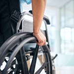 Hand, rehabilitation and person in a wheelchair at a hospital for medical support, transportation and mobility. Closeup, help and a patient with a disability in a chair at a clinic for recovery.