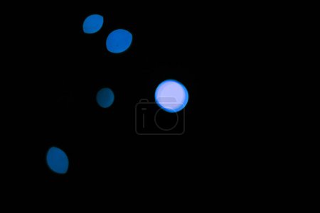 Foto de Bokeh, partículas de color azul neón sobre fondo negro y puntos con patrón, textura y maqueta con estética cósmica. Iluminación nocturna, luces brillantes y resplandor en el papel pintado oscuro con espacio, brillo y destello - Imagen libre de derechos