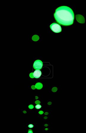 Foto de Bokeh, partículas verdes y luces sobre fondo negro con patrón, textura y maqueta con estética cósmica. Iluminación nocturna, puntos brillantes y brillo en el fondo de pantalla oscuro con espacio, brillo de color y destello. - Imagen libre de derechos