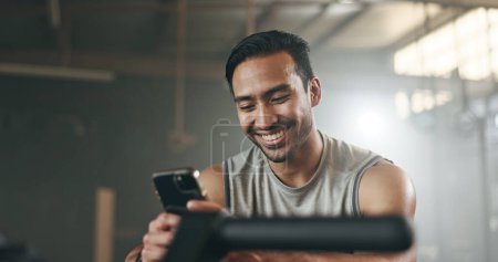 Photo for Happy asian man, phone and fitness on break in social media, communication or networking at gym. Active male person smile for online texting or chatting on mobile smartphone app at indoor health club. - Royalty Free Image