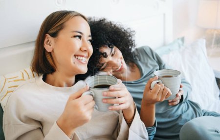 Photo for Coffee, communication and happy lesbian couple on bed bonding and relaxing together. Happy, rest and young interracial lgbtq women laughing, talking and drinking latte in bedroom of modern apartment. - Royalty Free Image