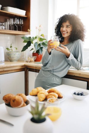 Photo for Woman, smile and thinking with orange juice in kitchen for breakfast, nutrition and vitamin c in the morning. Food, person and happiness with idea and drink with pajamas or natural face for wellness. - Royalty Free Image