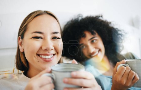 Téléchargez les photos : Café, sourire et portrait de couple lesbien sur le lit dans la conversation pour le lien et se détendre ensemble. Happy, repos et interracial femmes lgbtq rire, parler et boire latte dans la chambre à coucher de l'appartement - en image libre de droit