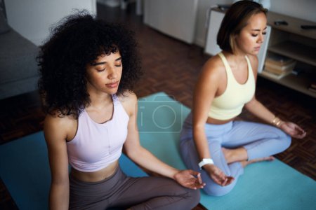 Foto de Pilates, fitness y amigas en la sala de estar haciendo una meditación en posición de loto juntas. Calma, paz y mujeres jóvenes haciendo ejercicio de yoga o ejercicio para respirar en el salón del apartamento. - Imagen libre de derechos