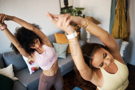 Téléchargez les photos : Yoga, étirements et copines dans le salon faisant un exercice de réchauffement ensemble pour le bien-être. Calme, la paix et les jeunes femmes faisant pilates séance d'entraînement pour respirer dans le salon de l'appartement moderne - en image libre de droit