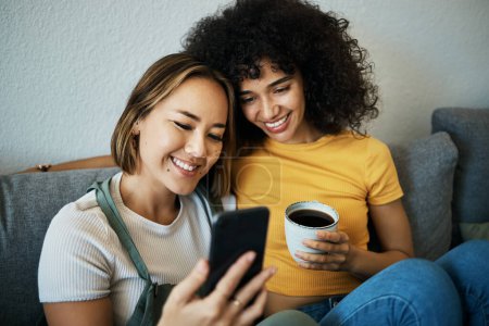 Photo for Lgbtq, sofa and couple relax with phone and coffee for social media, internet and watching videos. Love, home and happy women in living room for bonding, relationship and streaming movies online. - Royalty Free Image