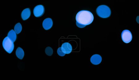 Téléchargez les photos : Bleu, lumières et bokeh dans un studio avec fond sombre pour la célébration, l'événement ou la fête. Confettis, paillettes et scintillements de couleur pour la magie, brillance ou lueur pour festive par fond noir avec maquette - en image libre de droit