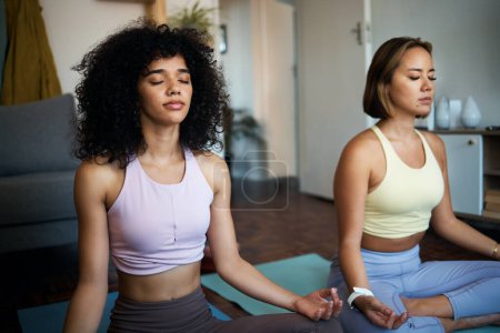 Photo for Meditation, yoga and girl friends in the living room doing fitness in lotus position together. Calm, peace and young women doing pilates workout or exercise for breathing in the lounge at home. - Royalty Free Image