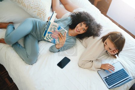 Photo for Laptop, morning and a lesbian couple relax in bed while together in their home on the weekend. Reading, computer and book with happy lgbt woman with her girlfriend in the bedroom from above for love. - Royalty Free Image