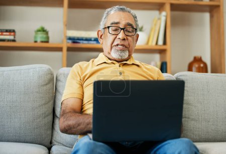 Photo for Typing, senior man and laptop on sofa in home with online research in living room or streaming video, movies or tv show. Elderly, person or writing on computer in retirement for blog or communication. - Royalty Free Image