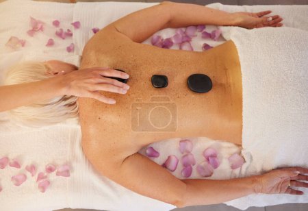 Photo for Woman, spa and above of stone massage for skincare treatment, holistic physical therapy and healing cosmetics at beauty salon. Relax, luxury wellness resort and hot rocks on back to detox muscles. - Royalty Free Image