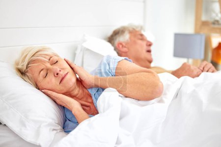 Photo for Snoring, problem and woman with frustrated with noise, sound or husband sleeping in bed with wife. Elderly, couple and man snore in sleep in retirement home bedroom and lady with hands on ears. - Royalty Free Image