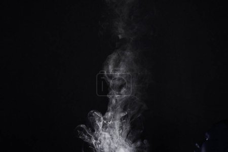 Téléchargez les photos : Fumée, vapeur ou gaz dans un studio avec un fond sombre par l'espace de maquette pour l'effet magique avec abstrait. Encens, vapeur ou brouillard se déplaçant dans l'air pour créer un smog nuageux sur fond noir avec maquette - en image libre de droit