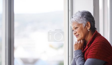 Photo for Lost in thought. Shot of a mature woman standing by a window on a sunny day - Royalty Free Image