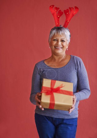 Photo for Heres a little something for you. Shot of a mature woman holding a gift and wearing festive reindeer antlers - Royalty Free Image