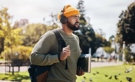 Téléchargez les photos : Homme sur le campus, marchant avec des livres et des écouteurs le matin de trajet pour l'éducation avec sac à dos. Apprendre, étudier et collégien dans le parc écouter du podcast, de la musique ou du streaming conférence en ligne. - en image libre de droit