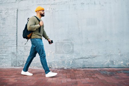 Photo for Student, walking and travel with man on wall, mockup and space in urban, campus or street in town. University, person and commute on path, road or journey to college in city with phone or backpack. - Royalty Free Image