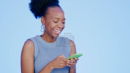 Téléchargez les photos : Téléphone, sourire et femme noire dans un réseau de studio sur les médias sociaux, application mobile ou Internet. Technologie, modèle féminin africain heureux et jeune défilement sur le site avec téléphone portable par fond bleu - en image libre de droit