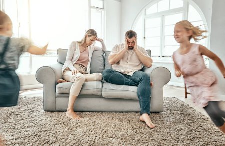 Photo for Frustrated couple, children and running in living room chaos with headache in stress on sofa at crazy or busy home. Parents in burnout with ADHD or hyper active kids or siblings playing wild in house. - Royalty Free Image