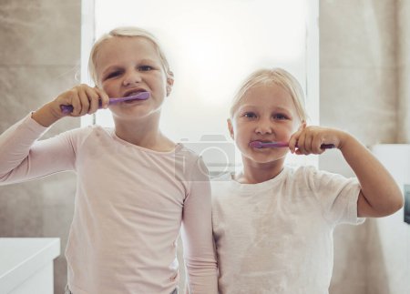 Foto de Niños, cepillarse los dientes y una niña con su hermana en el baño de su casa juntos para la higiene bucal. Retrato, limpieza dental y hermanos usando un cepillo de dientes en la mañana para el cuidado de la boca. - Imagen libre de derechos