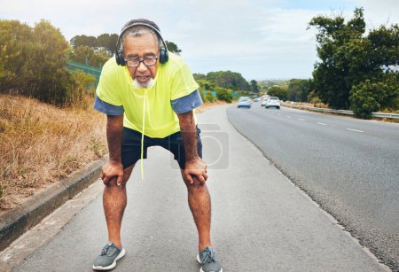 Photo for Tired, road and senior man with fitness, fatigue and exercise with wellness, workout and training. Runner, athlete and old person with headset, outdoor and exhausted with burnout, breathing and relax. - Royalty Free Image