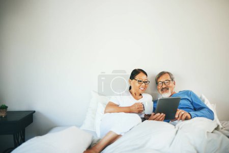 Photo for Tablet, senior or happy couple in bed on social media for communication on website or internet. People, bedroom or mature woman watching movie with an Asian man online streaming on technology at home. - Royalty Free Image