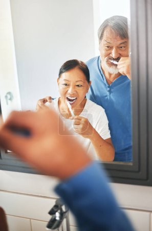Photo for Senior couple, brushing teeth and mirror in bathroom, hygiene and dental, morning routine at home. Healthy people, wellness and oral care with grooming, toothpaste for cleaning mouth and reflection. - Royalty Free Image