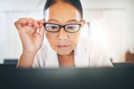 Photo for Mature woman, glasses and reading on computer for home blog or article on eye care, health and lens sale or discount. Business person with vision and laptop in work from home job or optometry website. - Royalty Free Image