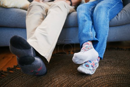 Photo for Legs, feet in socks and a couple on a sofa in the living room of their home together closeup to relax. Love, relationship and bonding with people in their house for a break on weekend in winter. - Royalty Free Image