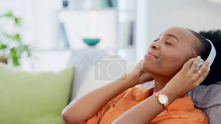 Foto de Auriculares musicales, relajarse o mujer negra en el sofá transmitiendo una canción o sonido tranquilo en la lista de reproducción de radio. Chica africana, la paz o la persona zen feliz escuchando un podcast de audio en la suscripción en el sofá de casa. - Imagen libre de derechos