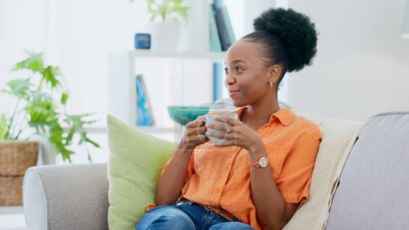 Photo for Black woman, smiling and sofa with hot beverage, relaxing and house for self care, lounge and break. Me time, comfort and quality time in home, lounge and day off for resting, laughing and happiness. - Royalty Free Image