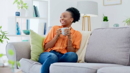 Photo for Black woman, smiling and couch with tea, relaxing and cozy home for self care, living room and break. Me time, comfort and quality time in house, sofa and day off for resting, laughing and happiness. - Royalty Free Image