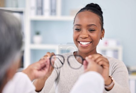Foto de Mujer negra, paciente y médico con gafas, cuidado ocular y consulta de visión con optometrista, cita y elección. Lente recetada, montura y ayuda con la sonrisa, consejos y optometría sanitaria. - Imagen libre de derechos