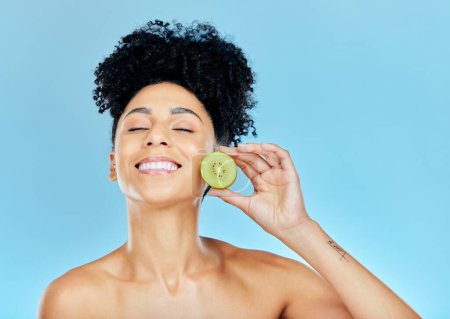 Photo for Smile, skincare and happy woman with kiwi in studio for wellness, detox or natural cosmetics on blue background. Face, glow and female model with fruit for beauty, nutrition or dermatology care. - Royalty Free Image