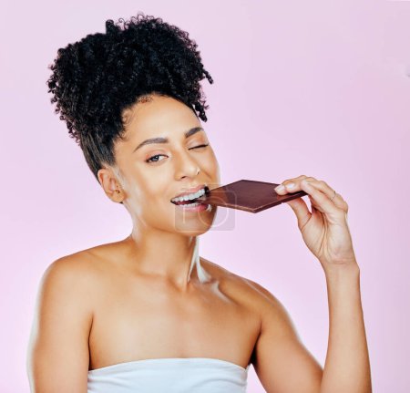 Photo for Portrait, sweet diet and woman with chocolate, eating and diabetes on a pink studio background. Face, person and model with unhealthy food, cacao treat and calories with sugar, nutrition and snack. - Royalty Free Image