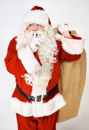 Photo for Santa claus, quiet and secret for present in studio for Christmas giving, festive season joy or fun. Male person, surprise emoji and sack or costume on white background, holiday or vacation break. - Royalty Free Image