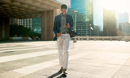 Photo for Business man, winner and phone in city for success, reading news or feedback of job opportunity or career goals. Happy african employee walking, travel and jump outdoor for winning and yes on mobile. - Royalty Free Image