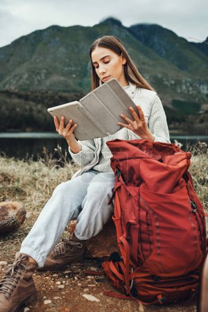 Photo for Tablet, reading and woman hiking with backpack in nature on mountain for adventure and weekend trip. Digital technology, bag and female person from Canada checking information and trekking in forest - Royalty Free Image