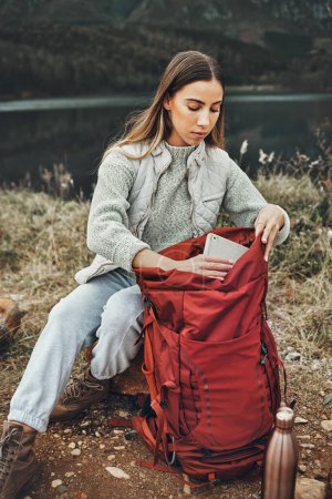 Photo for Woman, hiking and packing backpack in nature with tablet, check and thinking by lake, mountain or outdoor. Girl, luggage and trekking with bad, technology and ideas on adventure in countryside. - Royalty Free Image