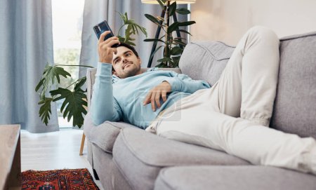 Photo for Man, phone and relax on sofa for social media, communication or entertainment in living room at home. Male person lying on lounge couch with mobile smartphone for online app or streaming at house. - Royalty Free Image