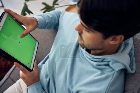 Foto de Tableta, pantalla verde y un hombre jugando en un sofá en la sala de estar de su casa desde arriba. Tecnología, juegos y jugadores jóvenes utilizando una pantalla o pantalla con marcadores de seguimiento para el entretenimiento. - Imagen libre de derechos